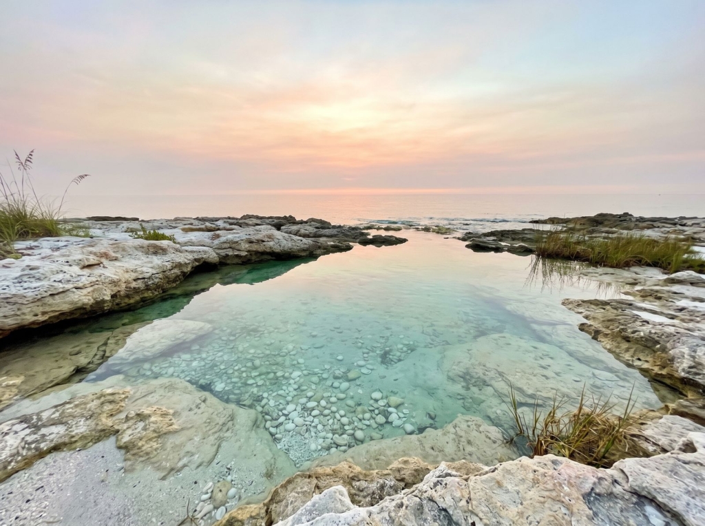 A clear, still tide pool among pale rocks with small white stones beneath the water